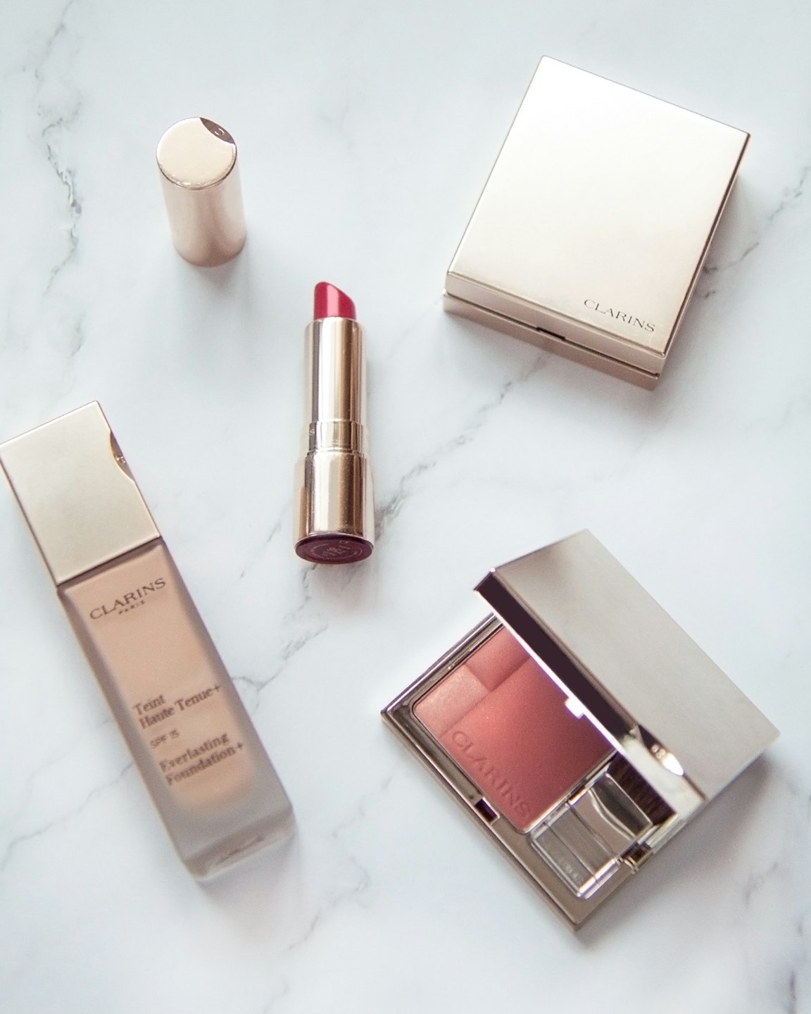 Four luxury makeup products arranged on white marble.